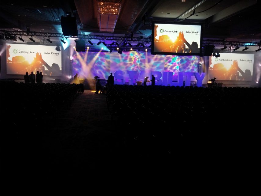 A corporate sales-kickoff stage lit in purple and gold, with large freestanding letters reading 'STABILITY'.