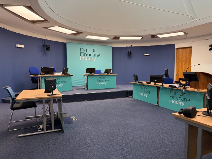 A broadcast hearing room fitted out for the Patrick Finucane Inquiry, with operator desks and screens.