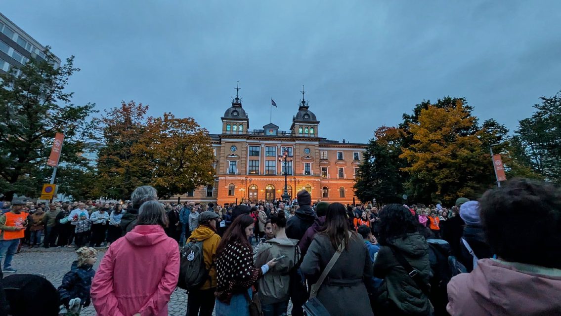 A crowd gathered in a town square at dusk for the Irish Festival of Oulu, with a historic building behind.
