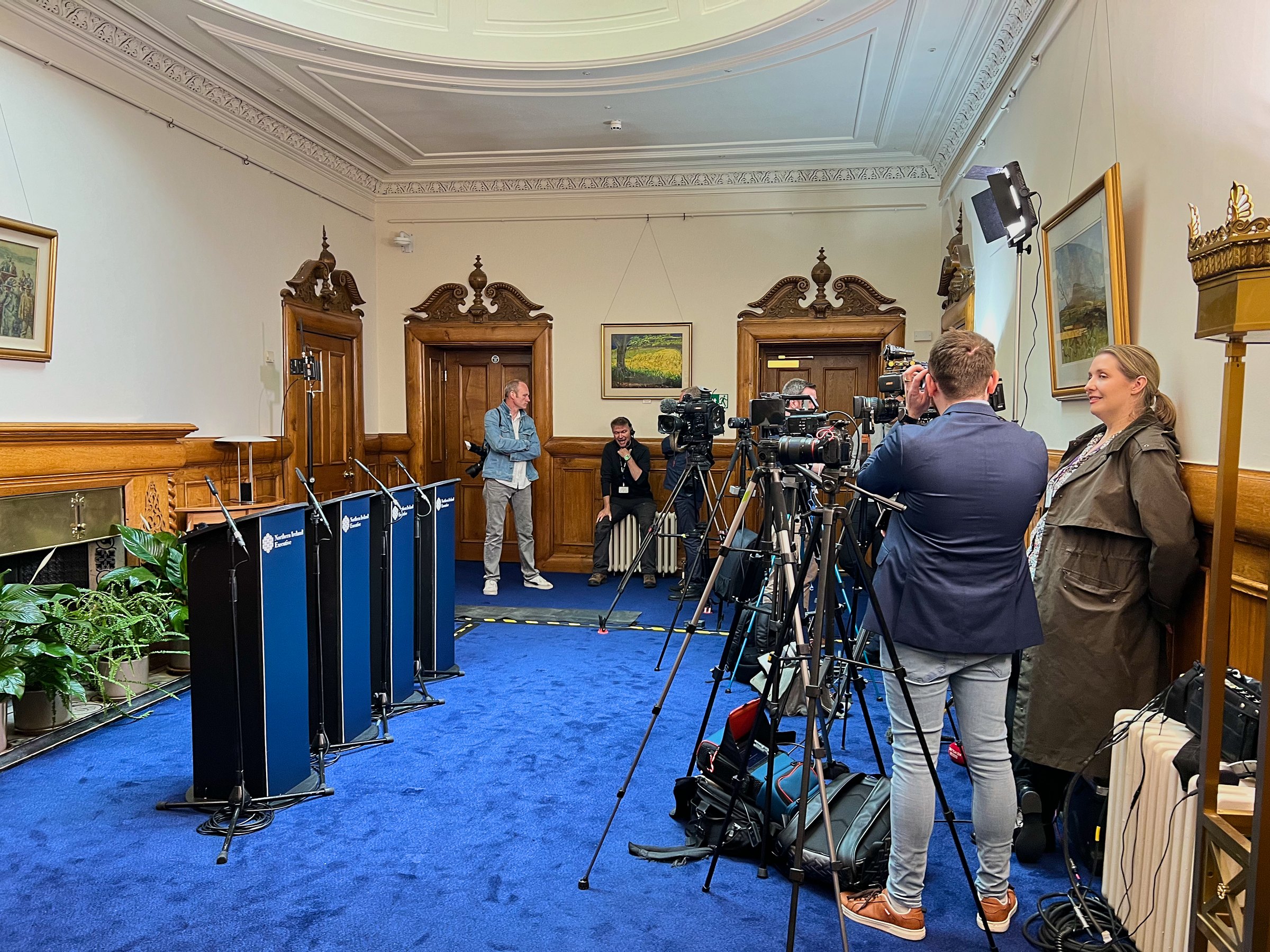 A broadcast camera crew and lighting setup in a wood-panelled committee room ahead of a press conference.